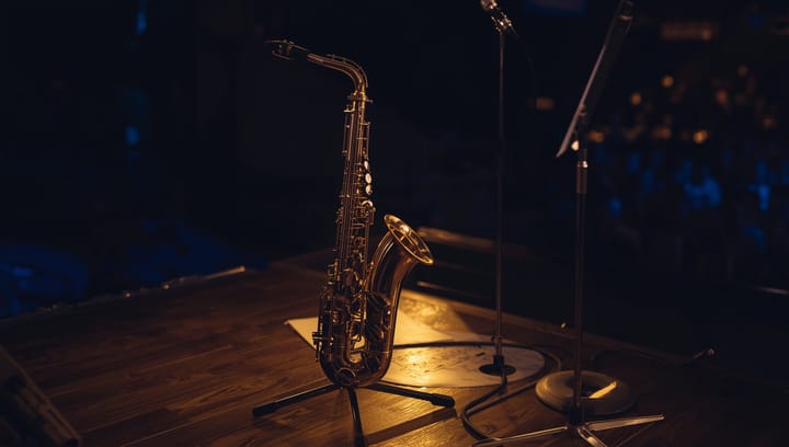 A saxophone stands upright in a silver saxophone stand on a wooden stage floor before the jazz concert begins.