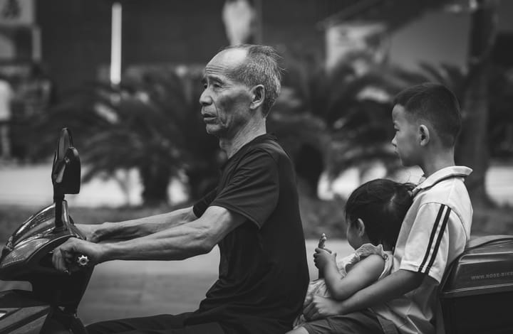 An older man with two children is riding a motorcycle.